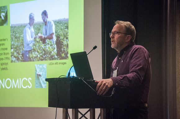 Speaker at podium with slides on screen in background