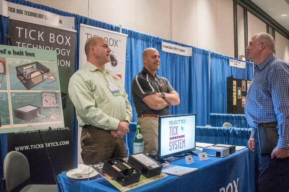 Three men speaking at an exhibit booth about ticks