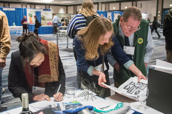 Two women and one man viewing auction items at display booth